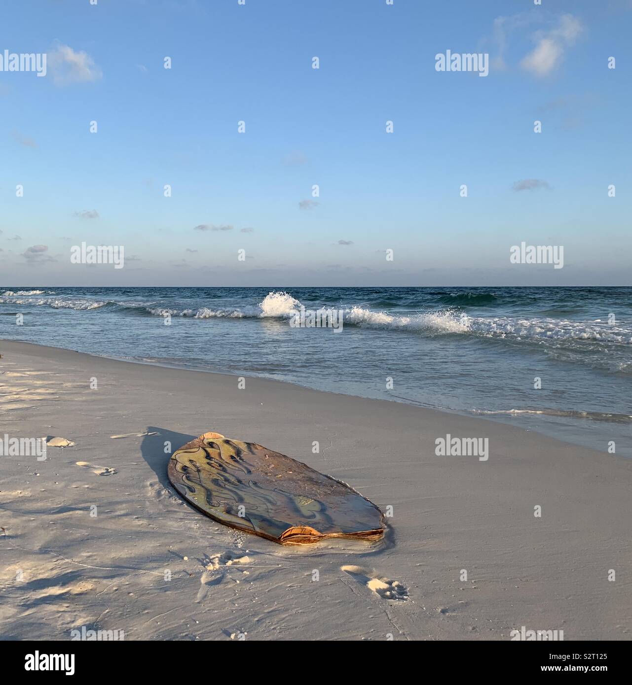 Washed up surf board on the beach with view of ocean water and skies at the start of sunset - Smartphone Captured Stock Image