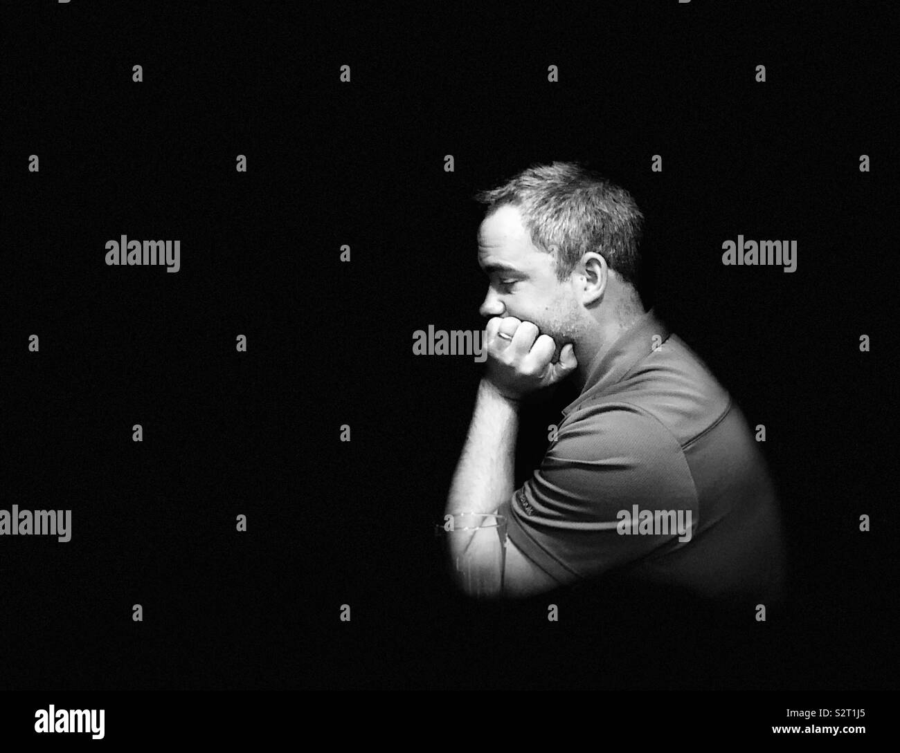 Man thinking with face resting on hand in darkness Stock Photo