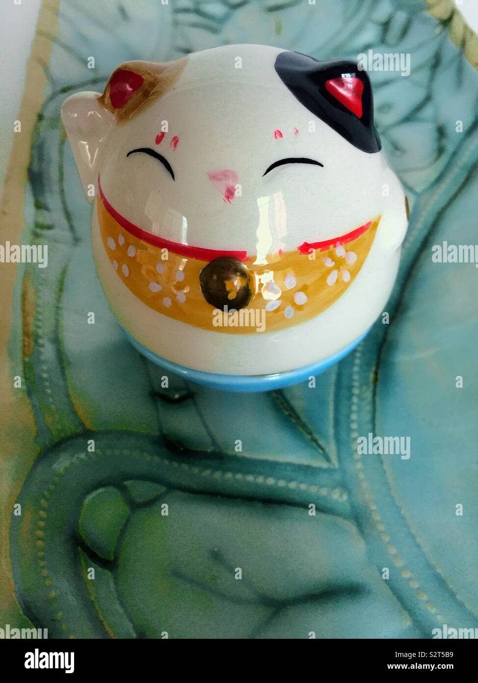 Close up of a cute Japanese lucky cat on a ceramic tray. Stock Photo