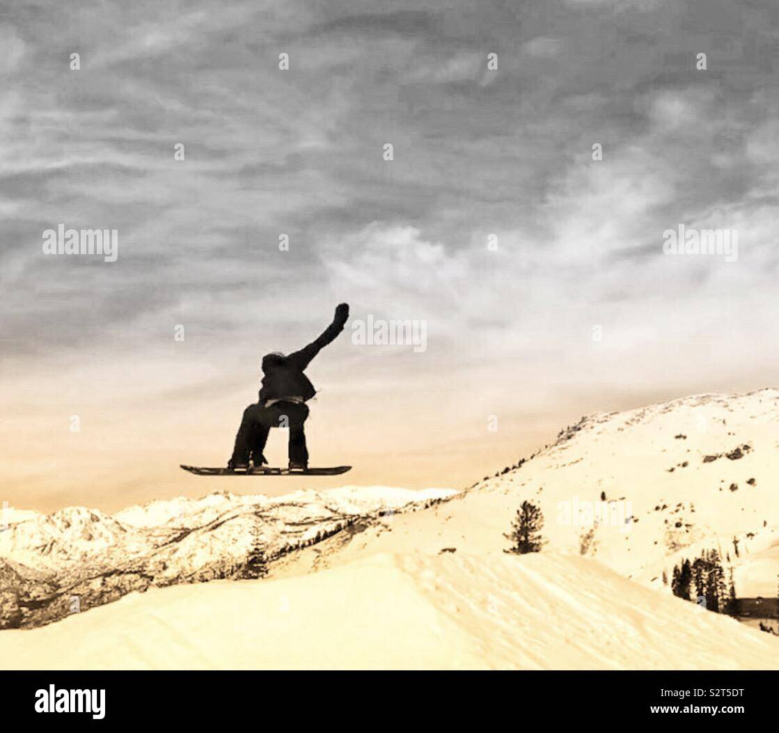 Bear Valley Ski Resort, Northern California. A snowboarder in the air doing a trick, grabbing his board one arm in air. Trees with snow in the background. Stock Photo