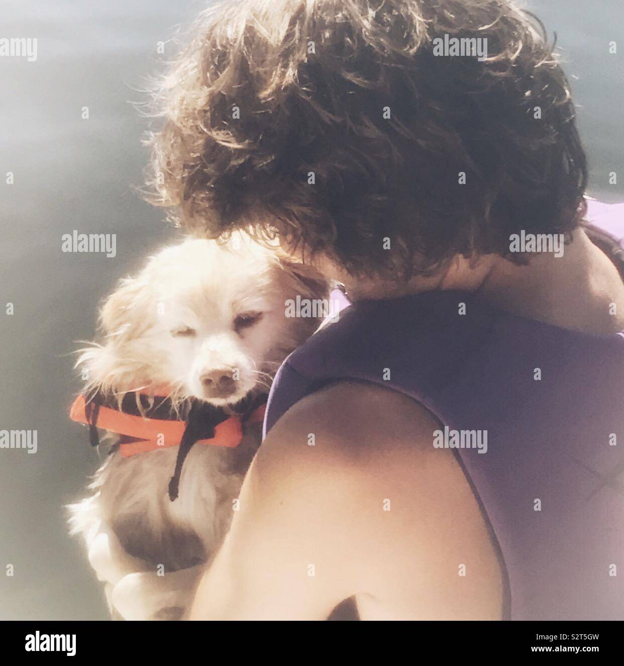 Boy and his dog boating. Boy and dog wearing life jackets and boy is holding dog close to his chest looking down on fluffy dog Stock Photo