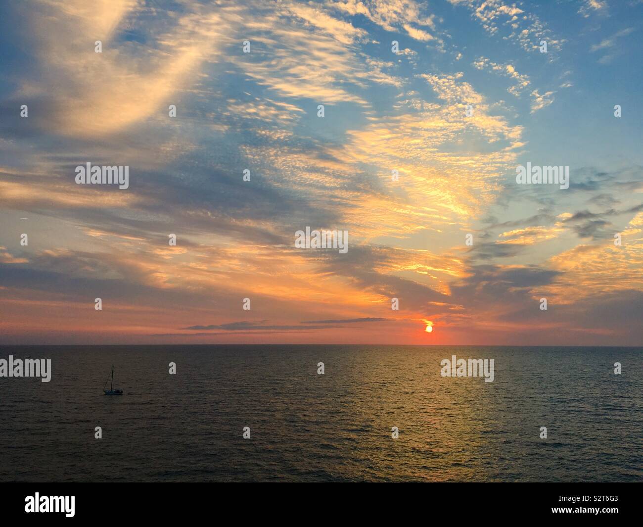 Sunrise over ocean with a sailing boat Stock Photo - Alamy