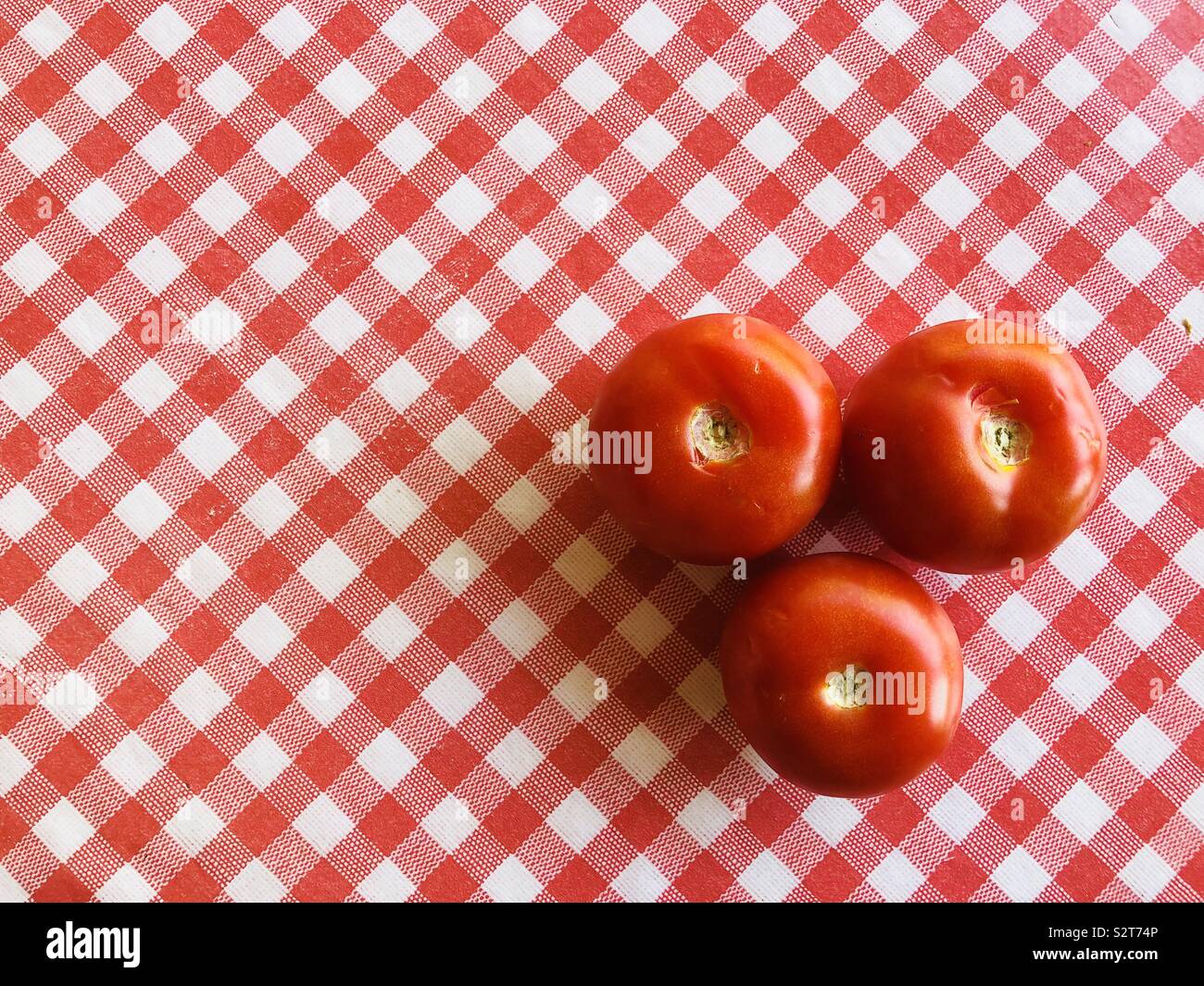 Three large tomatoes on red and white checked background Stock Photo