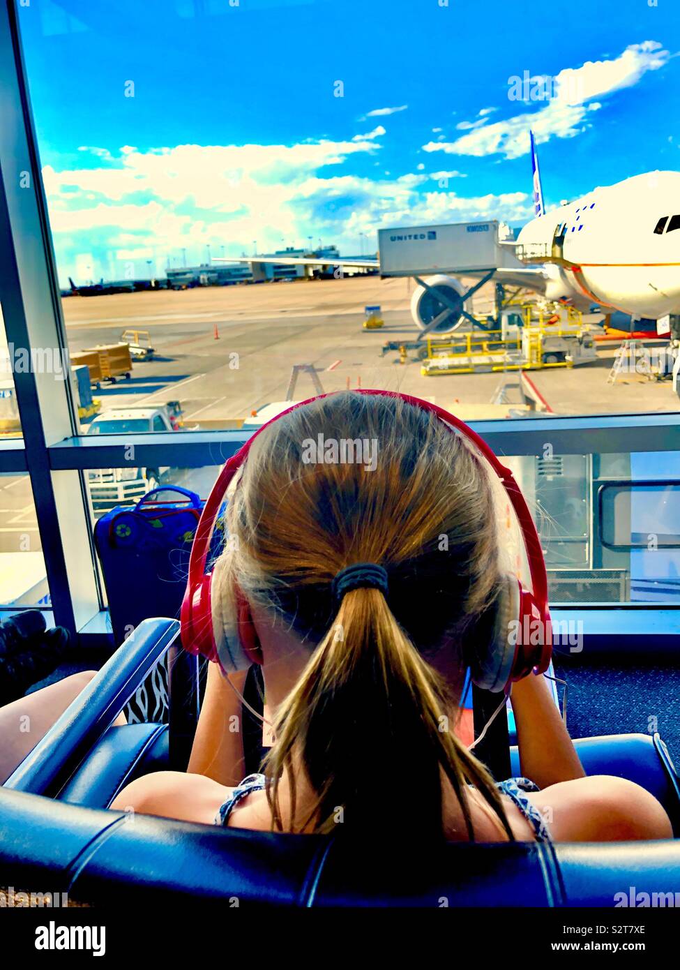 Teen girl at airport gate wearing headphones Stock Photo