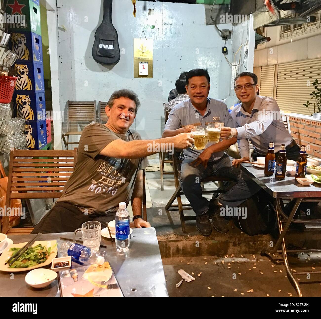 Caucasian tourist sharing a beer with locals in a Vietnamese restaurant in Ho Chi Minh City. Stock Photo