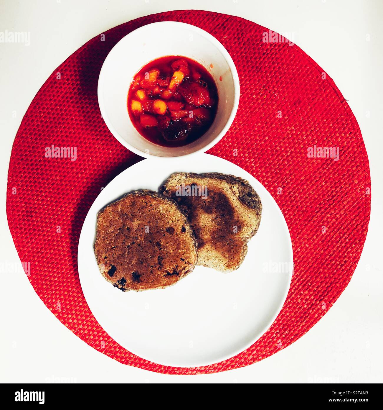 Vegan breakfast with oatmeal pancakes and peach and strawberry compote on red circle placemat - Smartphone Captured Stock Image