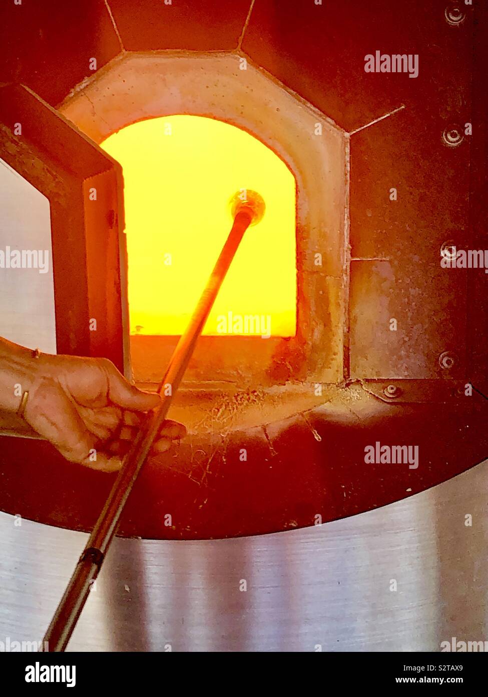 Molten glass on end of glass blowing rod being lifted out of the glory