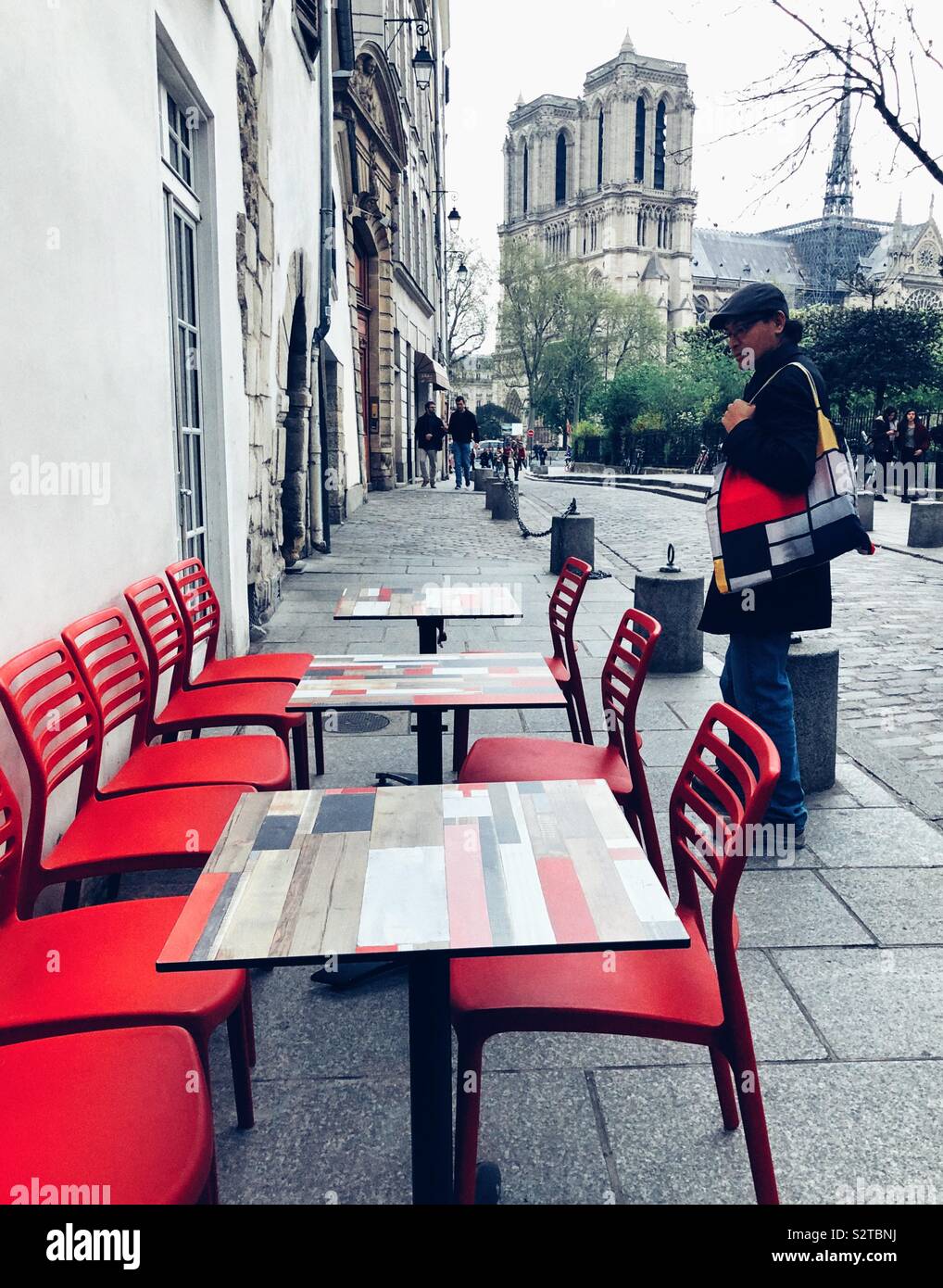 Man looks at colorful chairs and tables at outdoor cafe near Notre Dame Cathedral in Paris - Smartphone Captured Stock Image