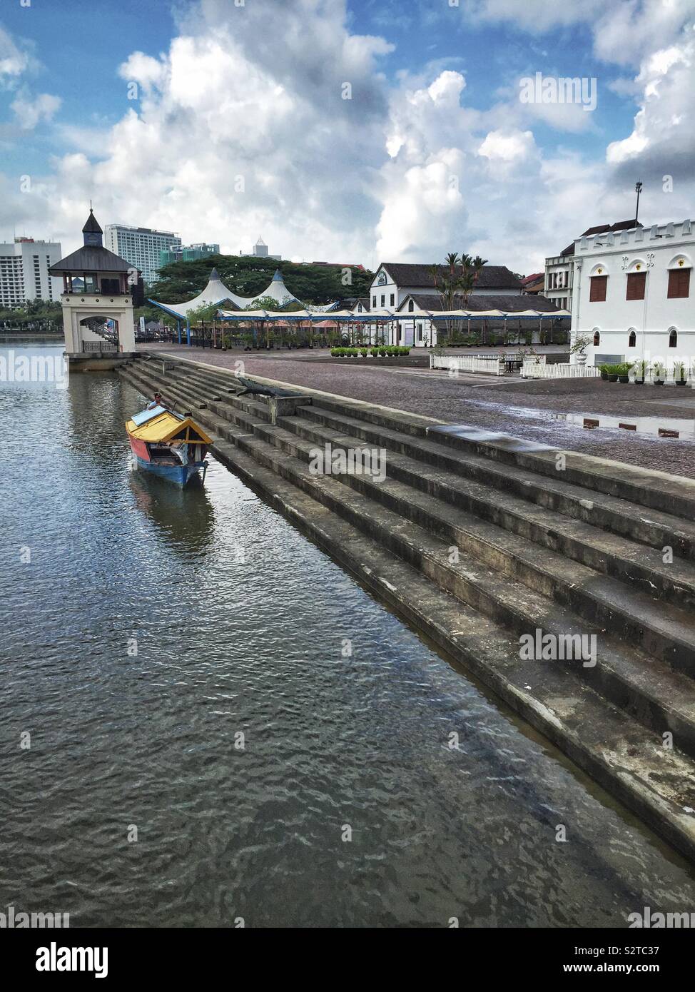 A boatman in his traditional Malay sampan waits to ferry people across the Sarawak River, near the Square Tower, an 1879 fort and prison, in the Waterfront precinct, Kuching, Sarawak, Malaysia - Smartphone Captured Stock Image