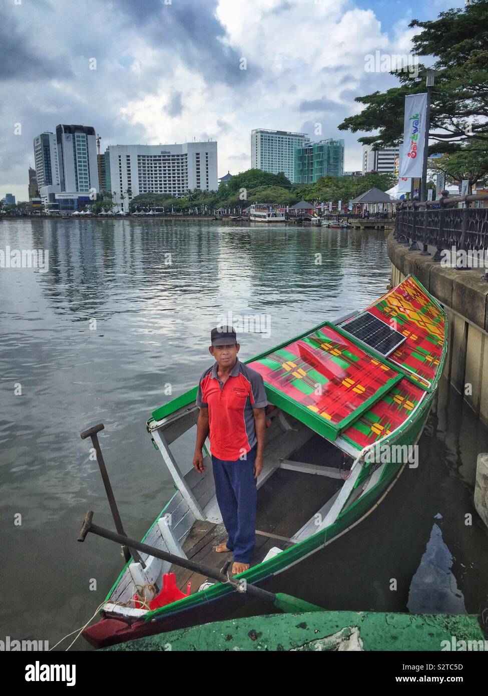 A boatman and his traditional Malay sampan, modernised with solar panels for an electric motor, used to ferry people across the Sarawak River, Kuching, Sarawak, Malaysia Stock Photo