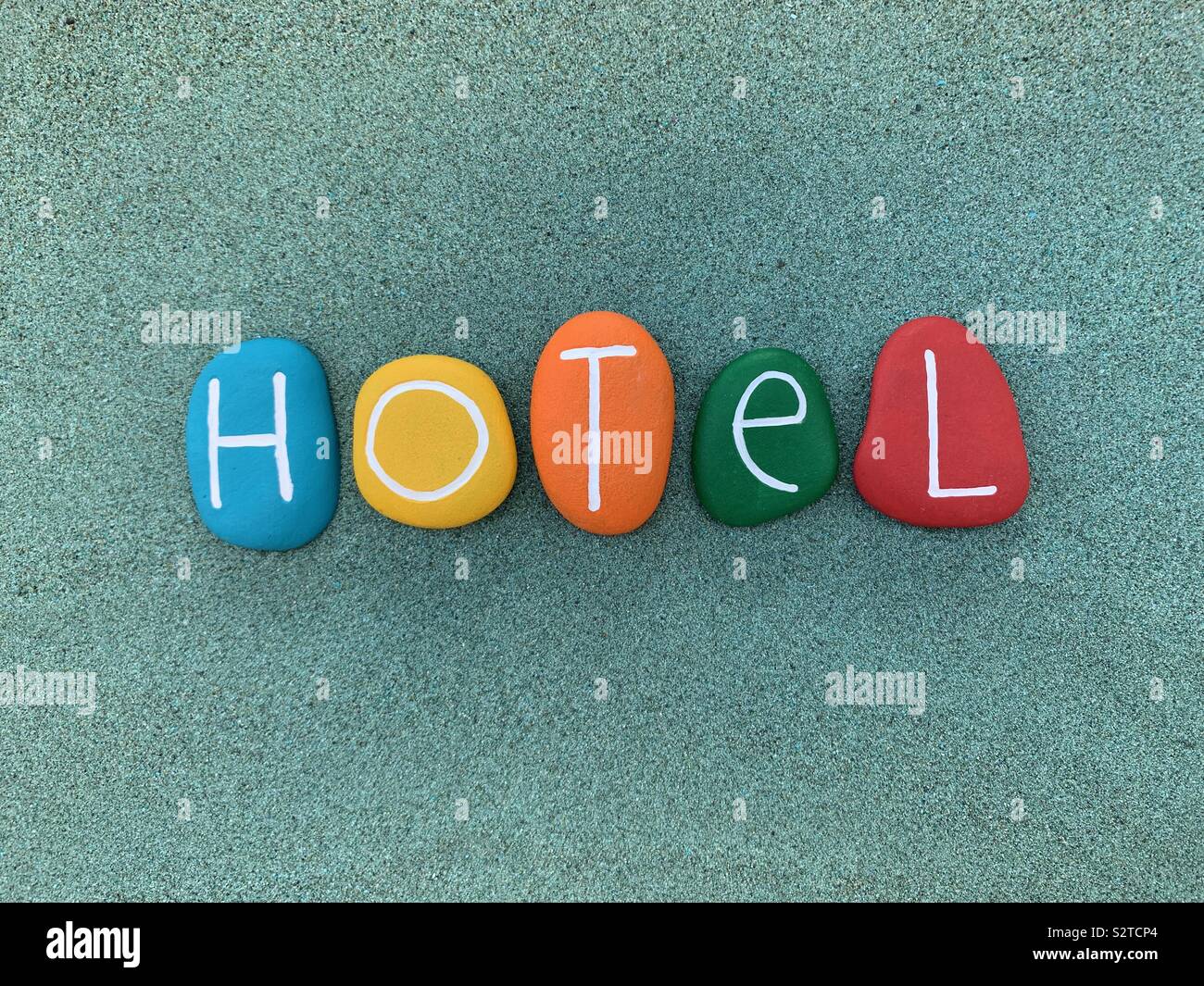 Hotel text composed with colored stones over green sand - Smartphone Captured Stock Image