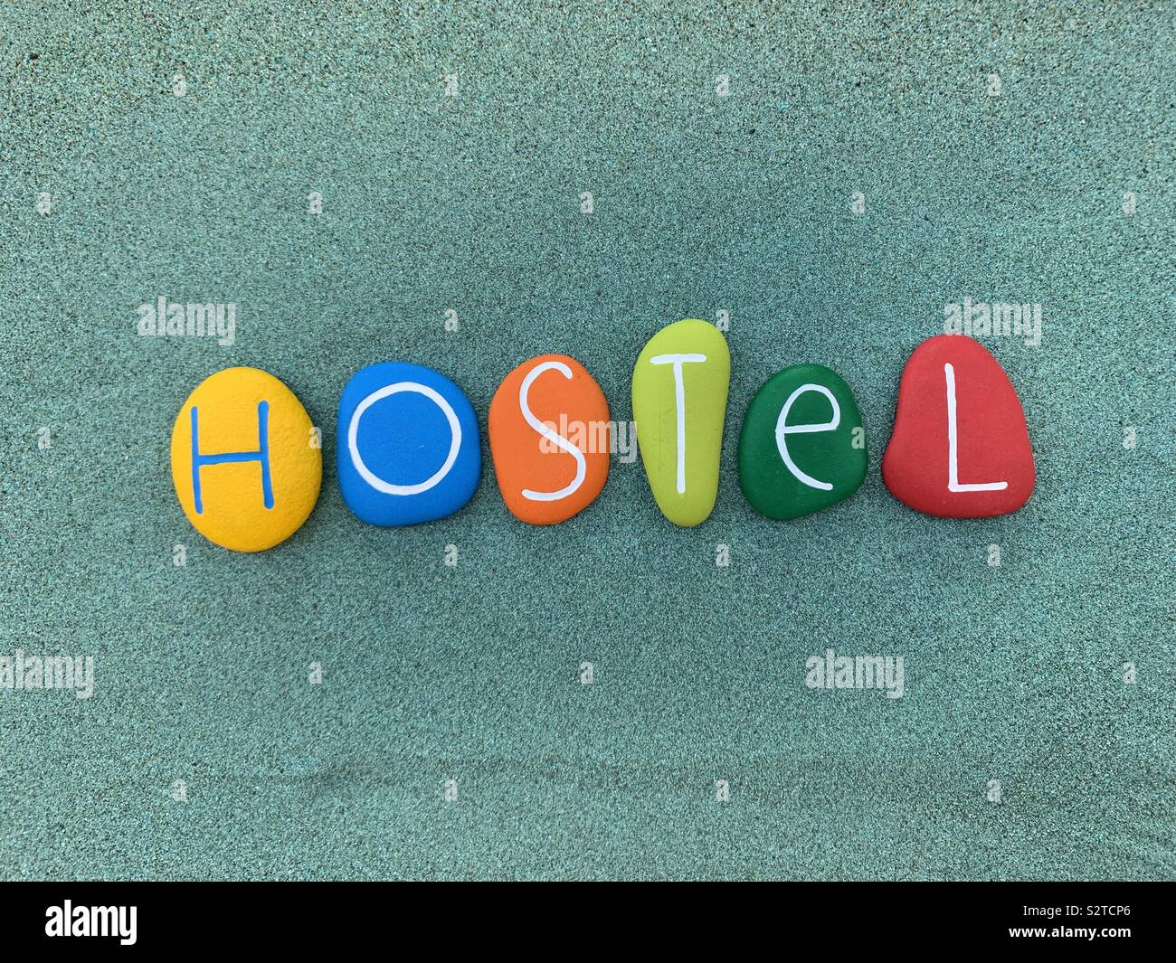 Hostel text composed with multicolored stones over green sand - Smartphone Captured Stock Image