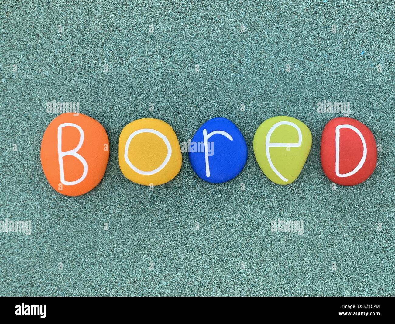 Bored word composed with colored stones over green sand - Smartphone Captured Stock Image