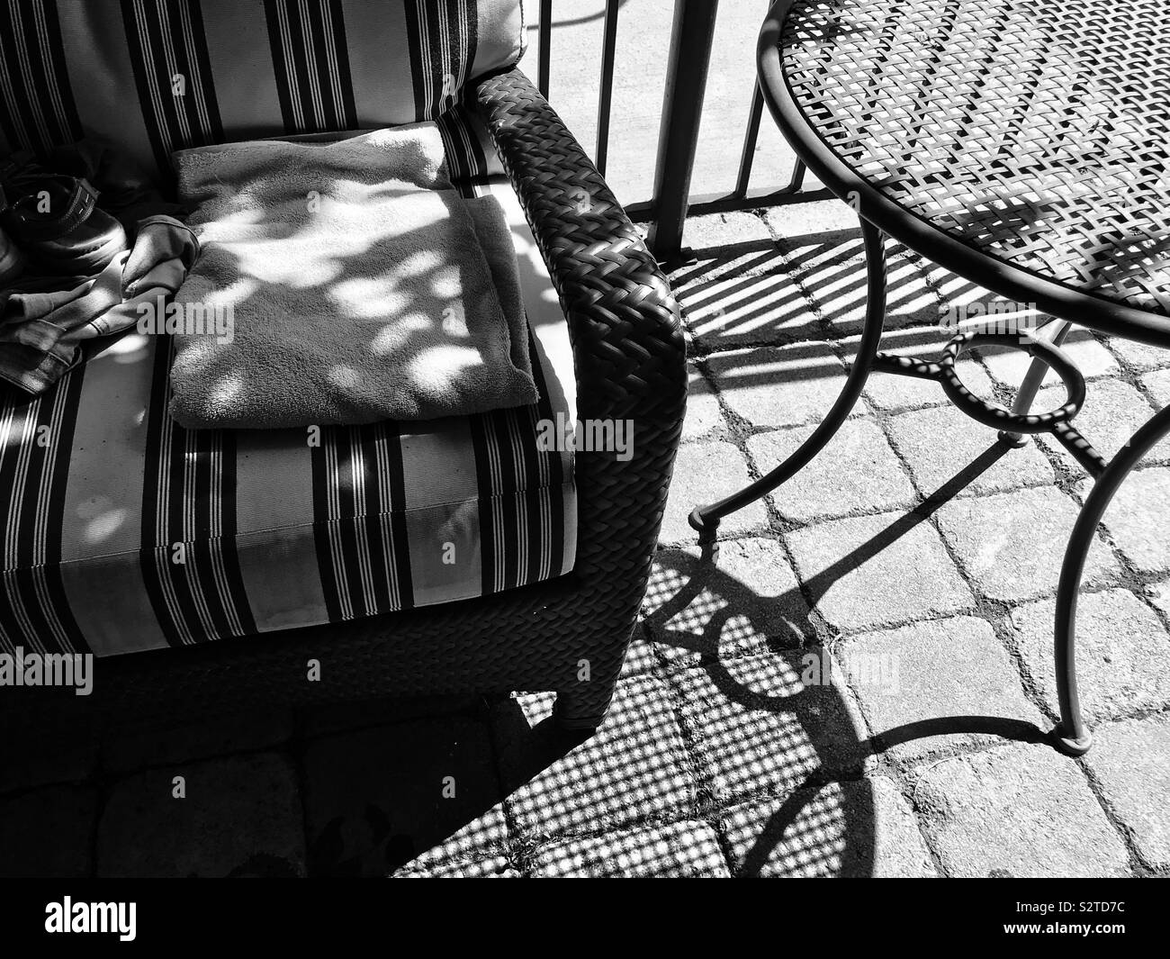 Black and white photo of patio by poolside with shadows, towel, and clothing of swimmer - Smartphone Captured Stock Image