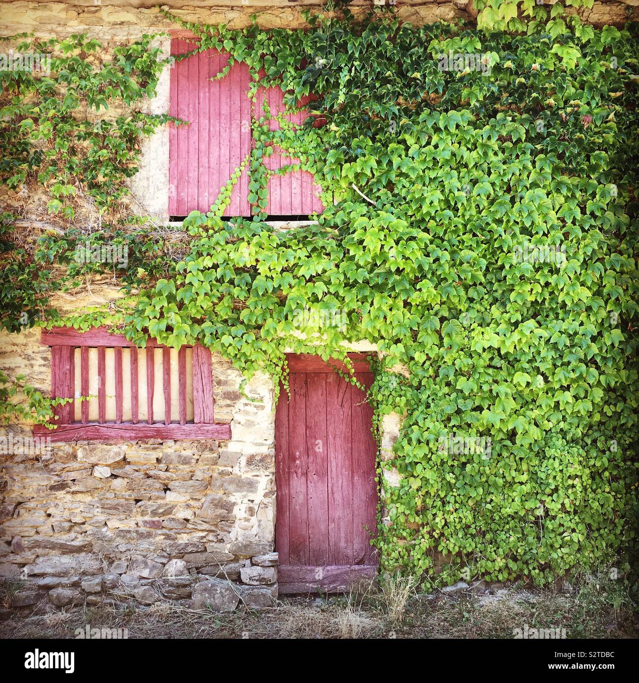 Detail of an old stone house facade with burgundy red wooden door and ...