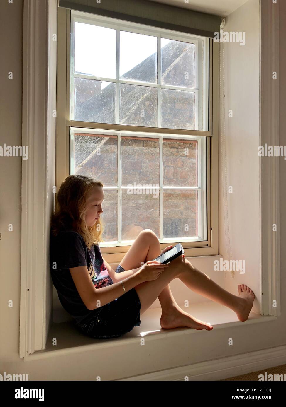 Girl reading a book on a wooden window seat Stock Photo