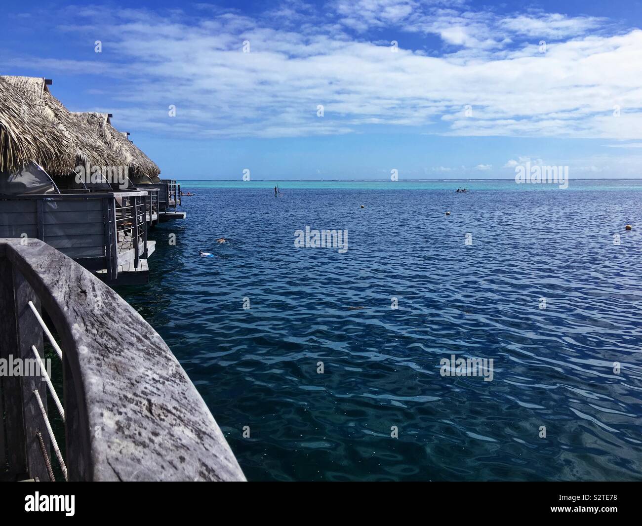 View from the balcony of an overwater bungalow in a resort on Moorea, French Polynesia. Two snorkelers are in the water, there is a person paddle boarding, and four people in two kayaks. - Smartphone Captured Stock Image