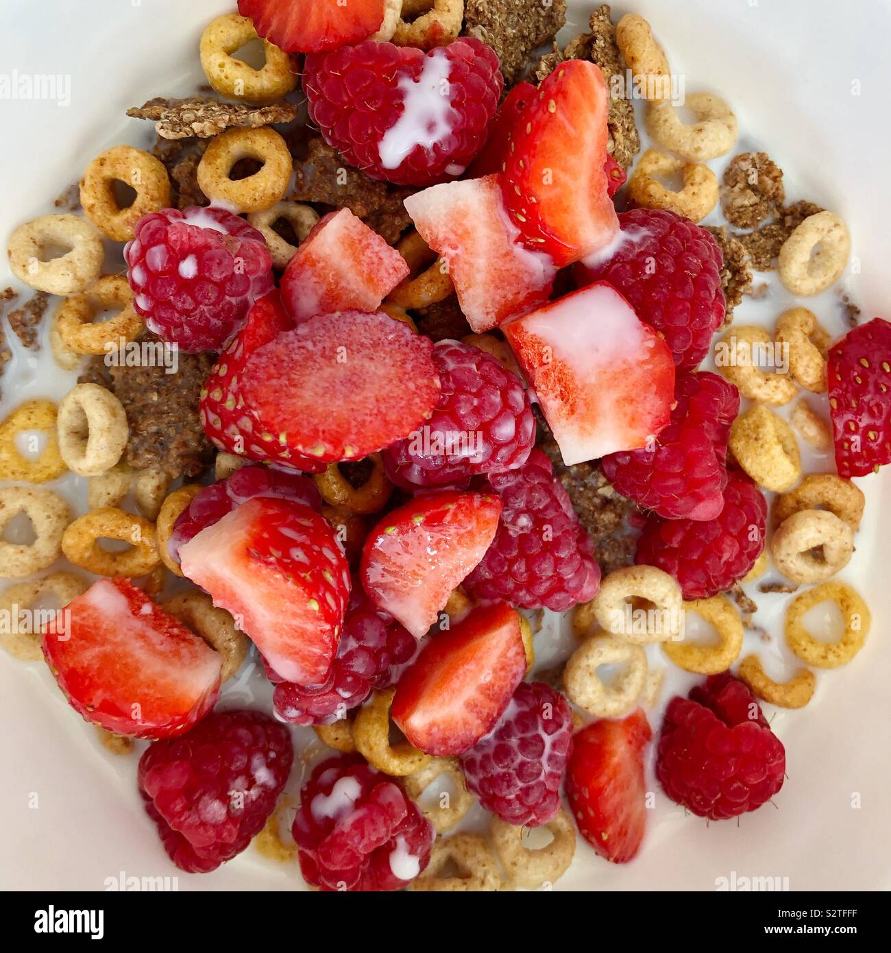 Closeup of bowl of breakfast cereals and fruits with milk seen from