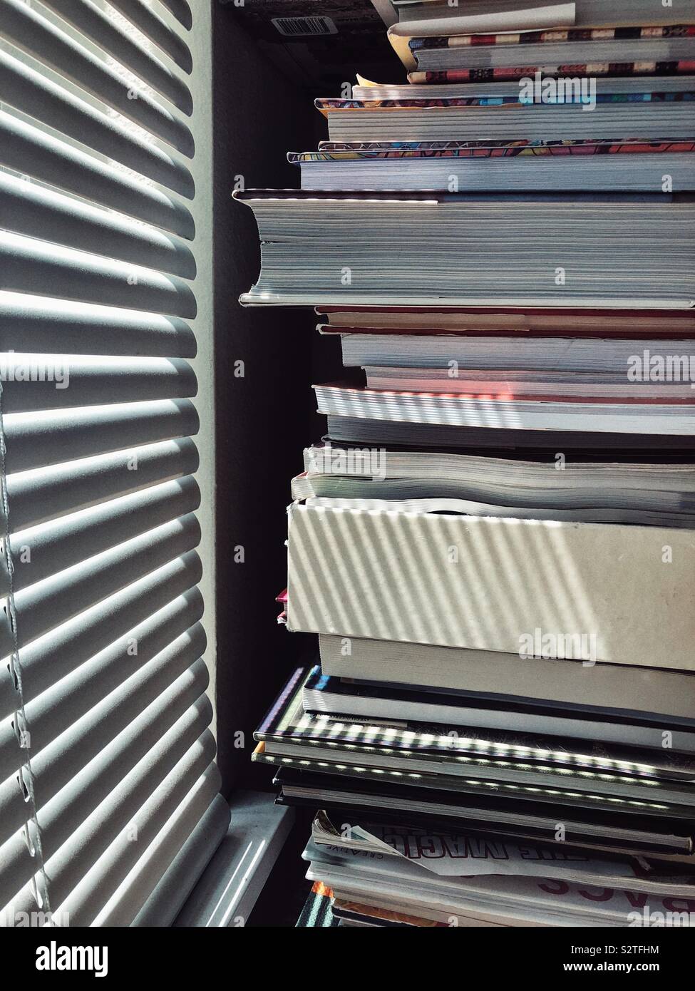Books piled up near window with blinds Stock Photo