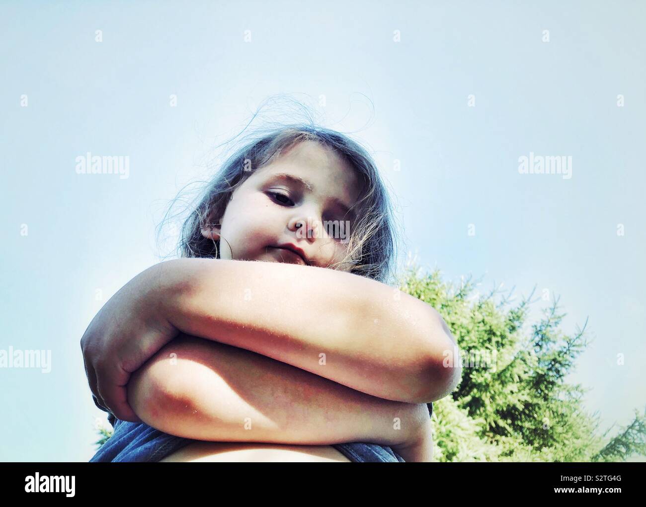 Looking up at young girl with crossed arms and disapproving expression Stock Photo