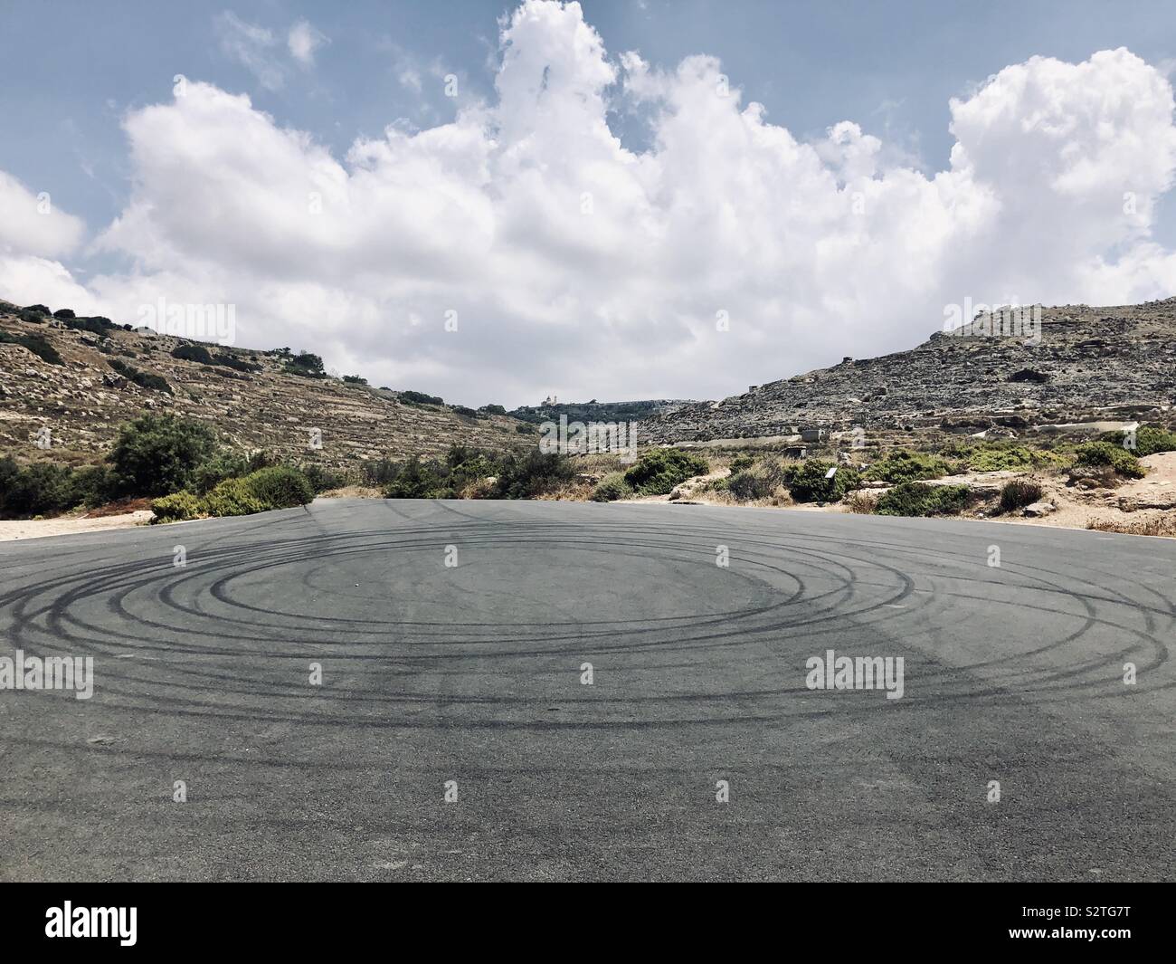 Doughnut skid rings on tarmac in Malta with clouds and hills in the background Stock Photo