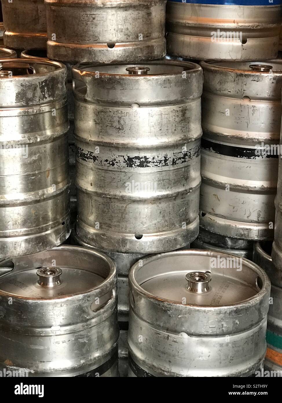 Many generic, used, and scuffed metal beer kegs are shown stacked in a brewery in a vertical view. - Smartphone Captured Stock Image