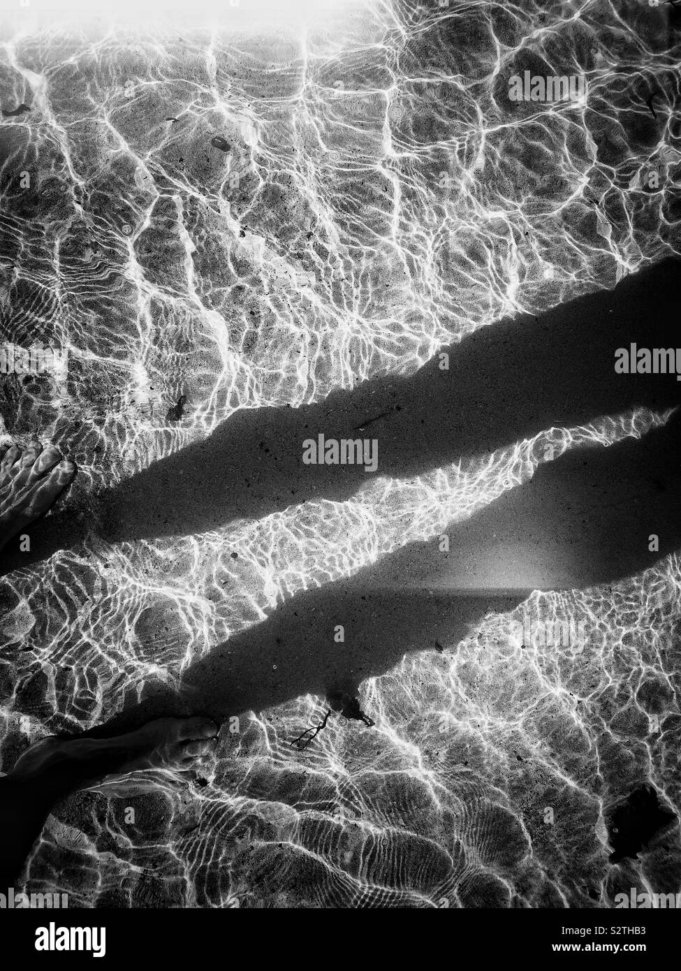 Strong contrast black and white image of shadow of man standing in clear sunlit rippled ocean - Smartphone Captured Stock Image