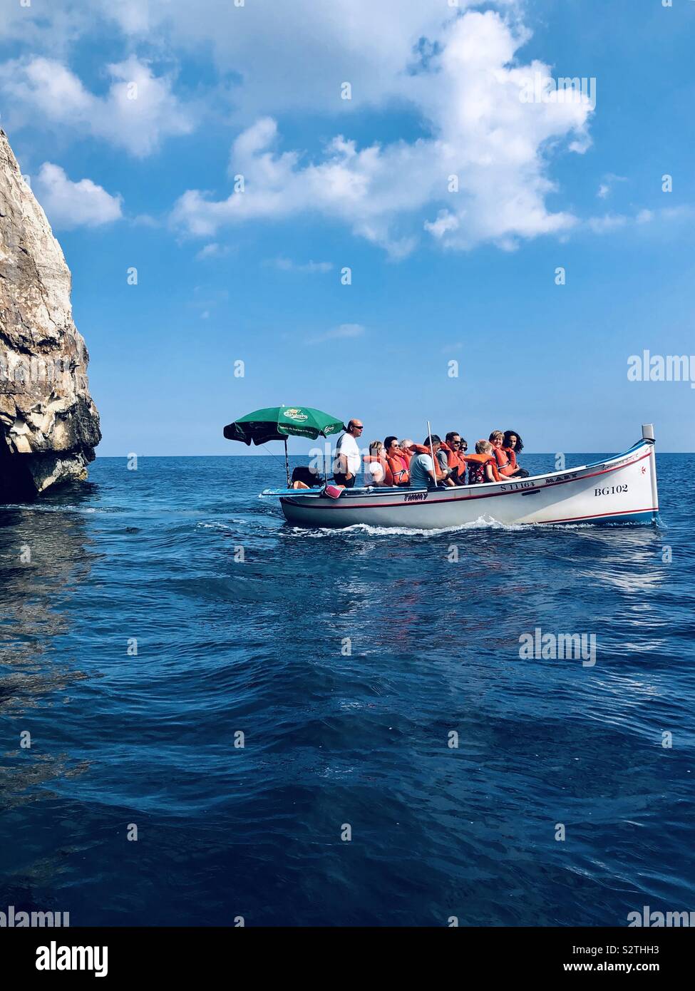 Tourists in life vests in a small boat near the blue cave in Malta Stock Photo