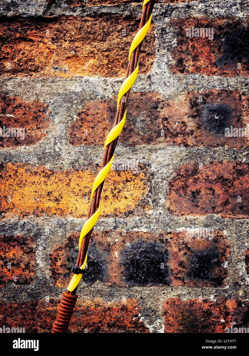 Wire entwined with yellow plastic against a red brick wall. Stock Photo
