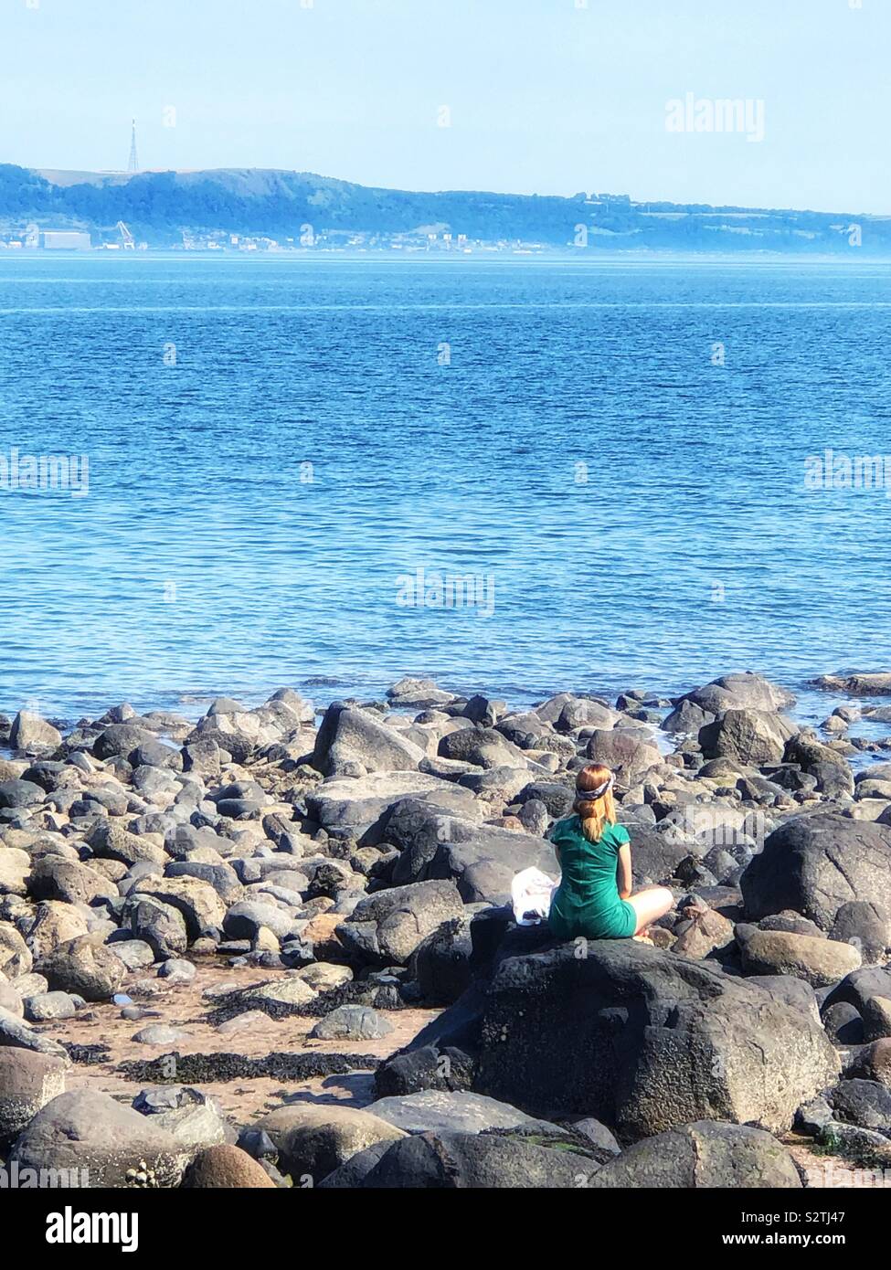 Woman sitting on coastal rocks hi-res stock photography and images - Alamy