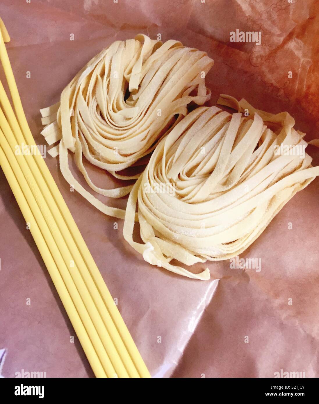Knots of fresh tagliatelle Pasta on wax paper next to a pasta fork - Smartphone Captured Stock Image