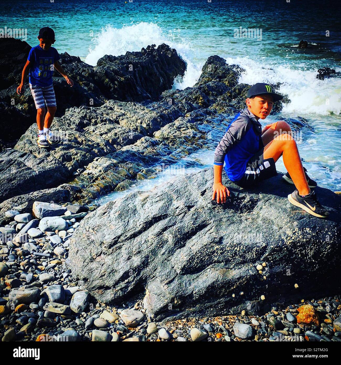 2 young friends or brothers playing on rocks near the sea or icean Stock Photo