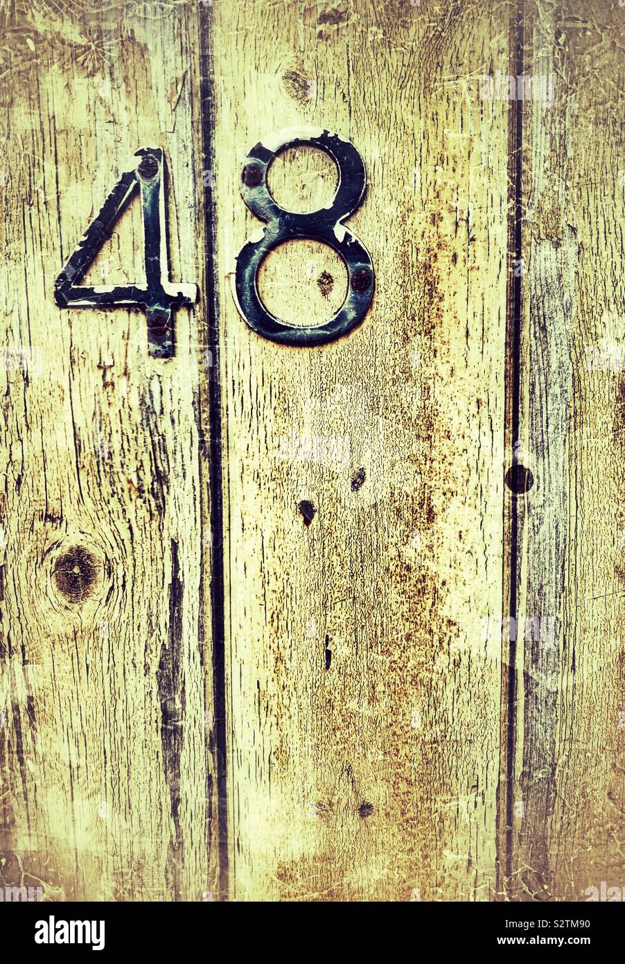Worn metal number  forty eight on grainy wood panelled door Stock Photo