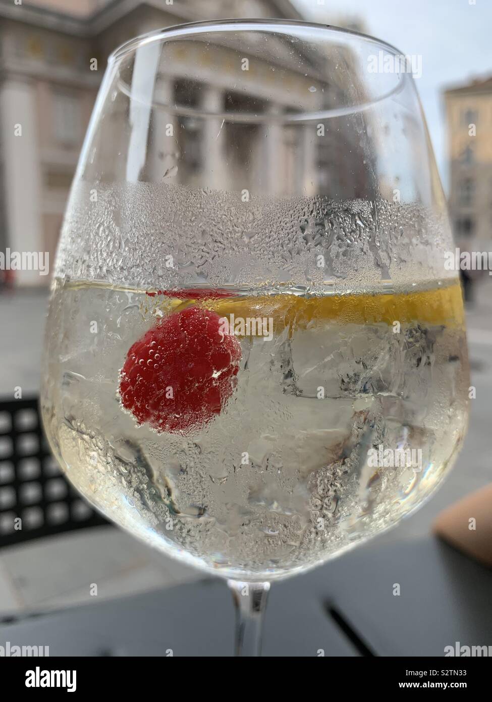 Glass of white wine spritz. Stock Exchange building in the background. Trieste, Italy. - Smartphone Captured Stock Image
