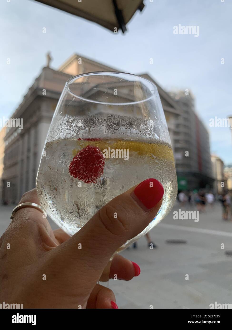 Woman hand raising a glass of white wine spritz in front of historical Stock Exchange building in Trieste, Italy. - Smartphone Captured Stock Image
