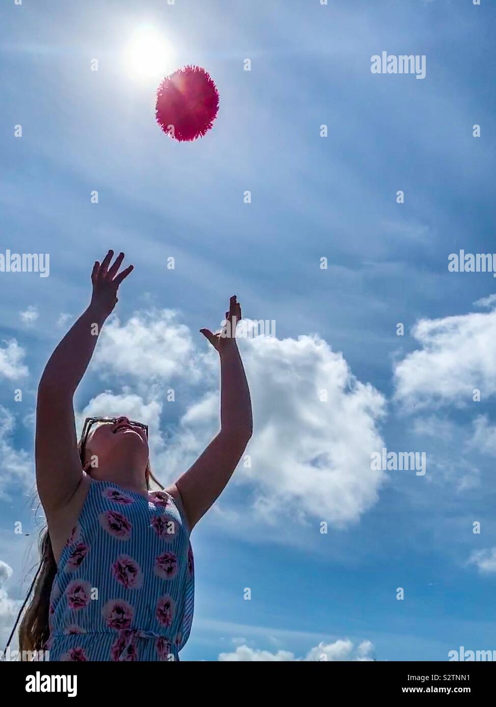 Young girl throwing a pink ball in sky Stock Photo