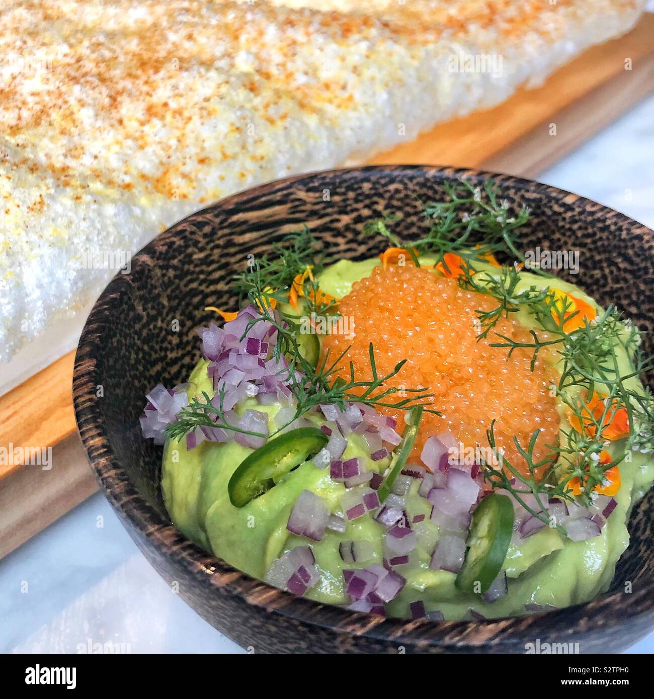 A closeup of a bowl of avocado guacamole and orange caviar near a large rice cake Stock Photo