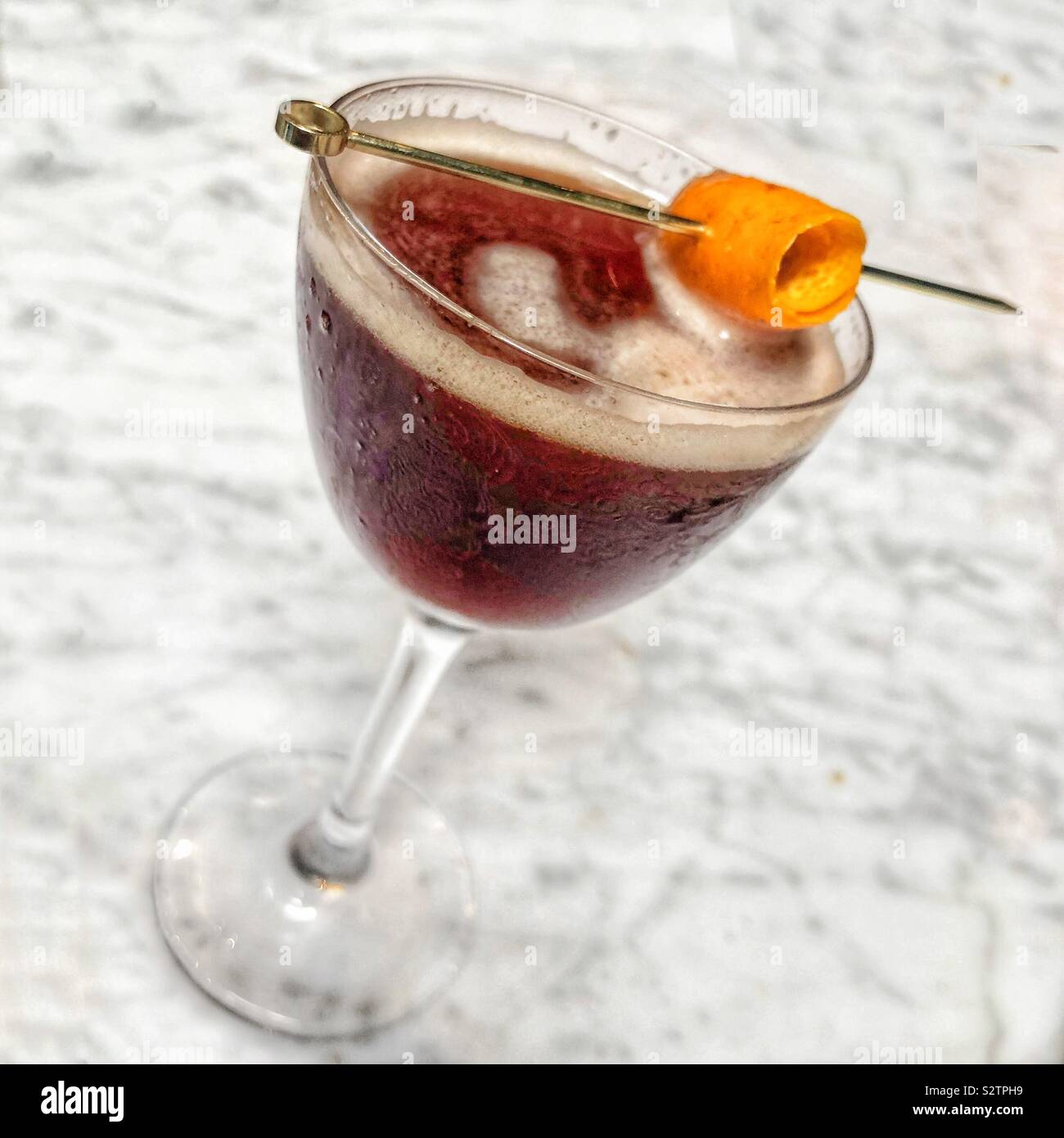 A cocktail drink with an orange peel garnish on a white marble background - Smartphone Captured Stock Image