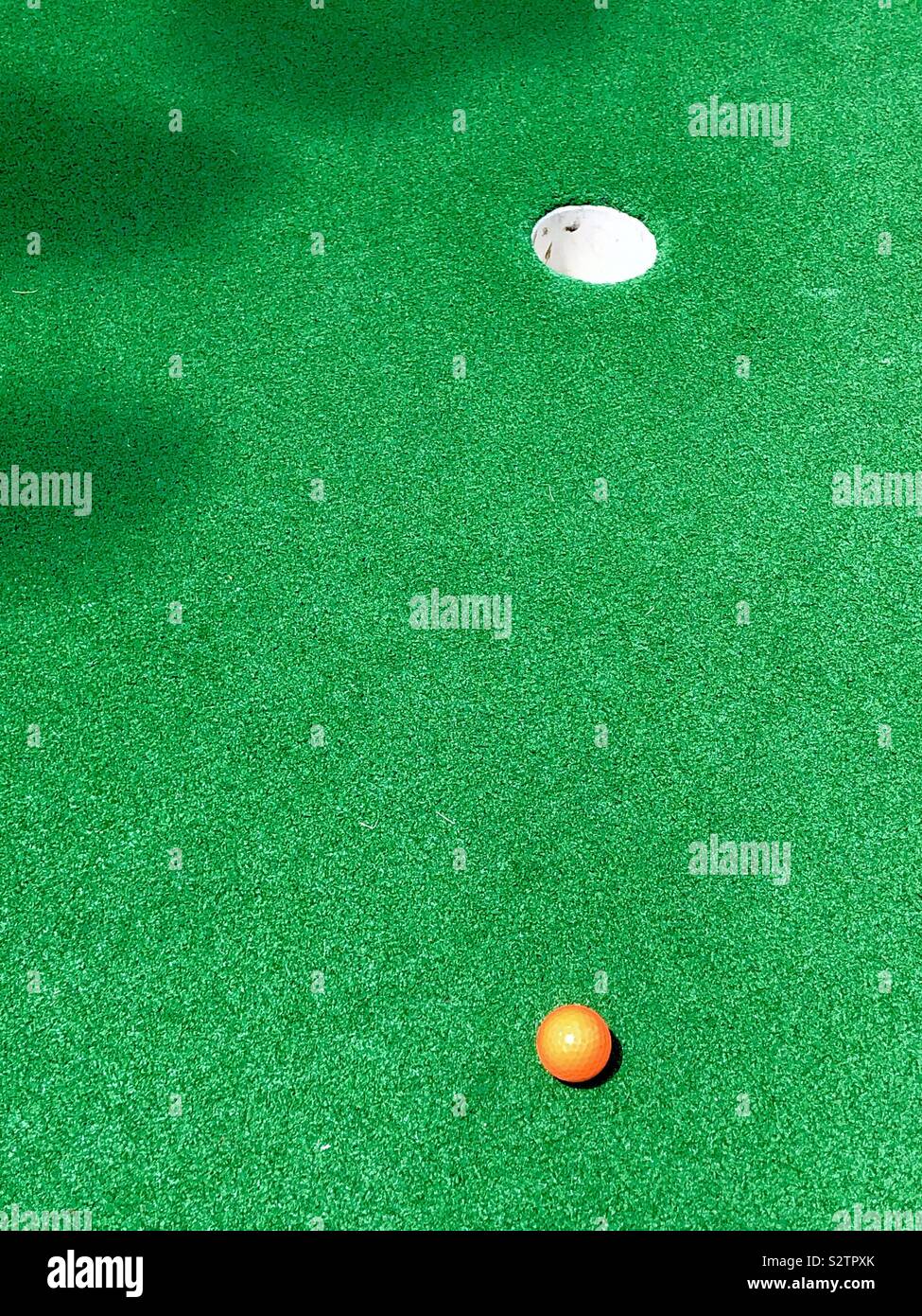 Mini golf putt-putt miniature orange golf ball on green away from cup Stock Photo