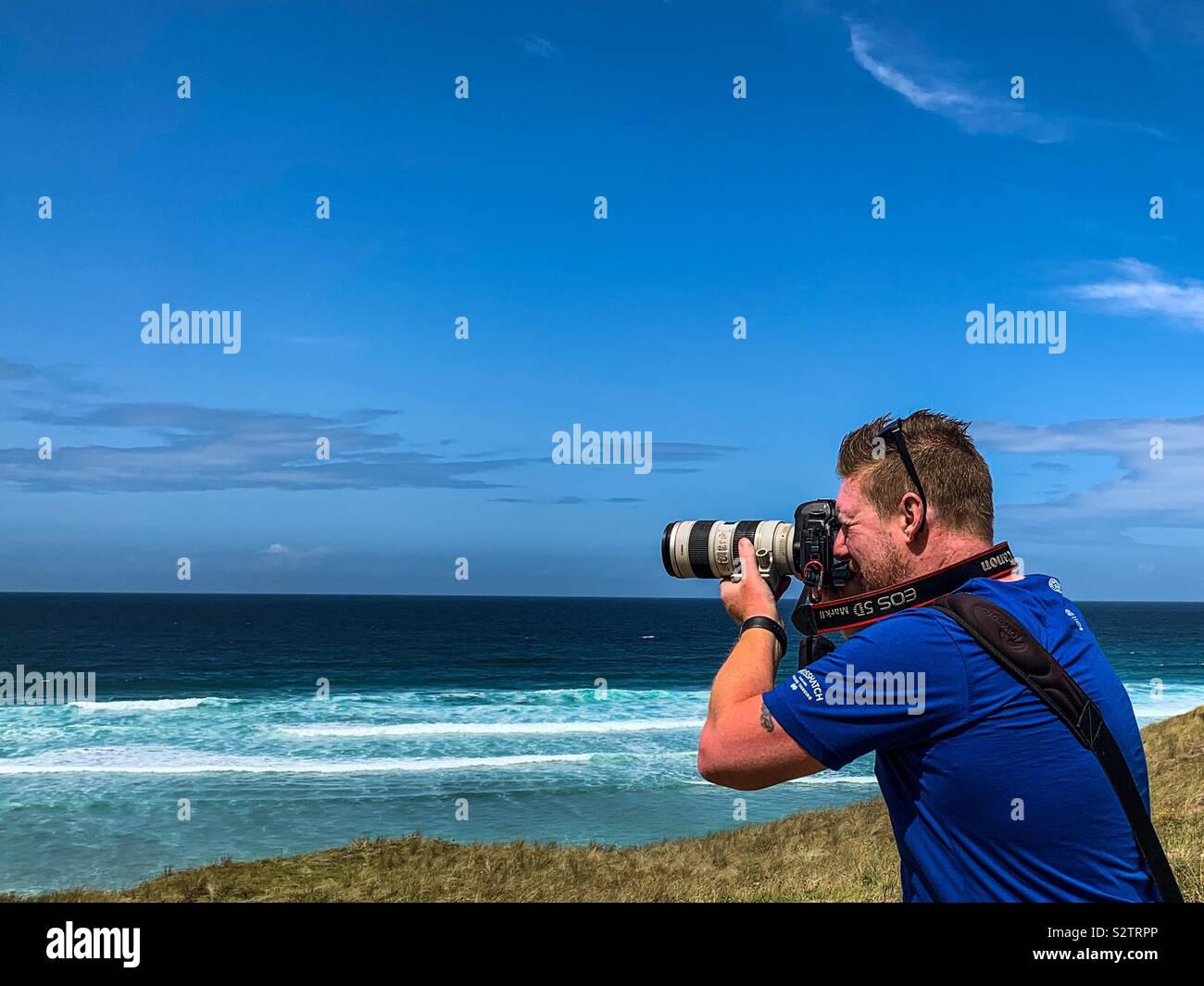 Man taking photos on cliffs at perran sands beach in Perranporth Cornwall - Smartphone Captured Stock Image