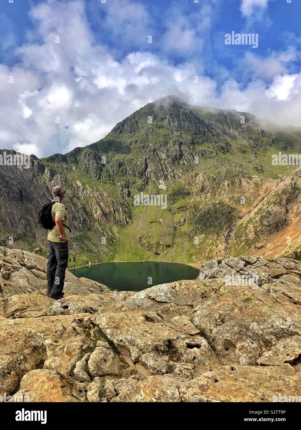 A middle aged man looking up at the cloud capped peak of Snowdon from Glaslyn lake, August. - Smartphone Captured Stock Image