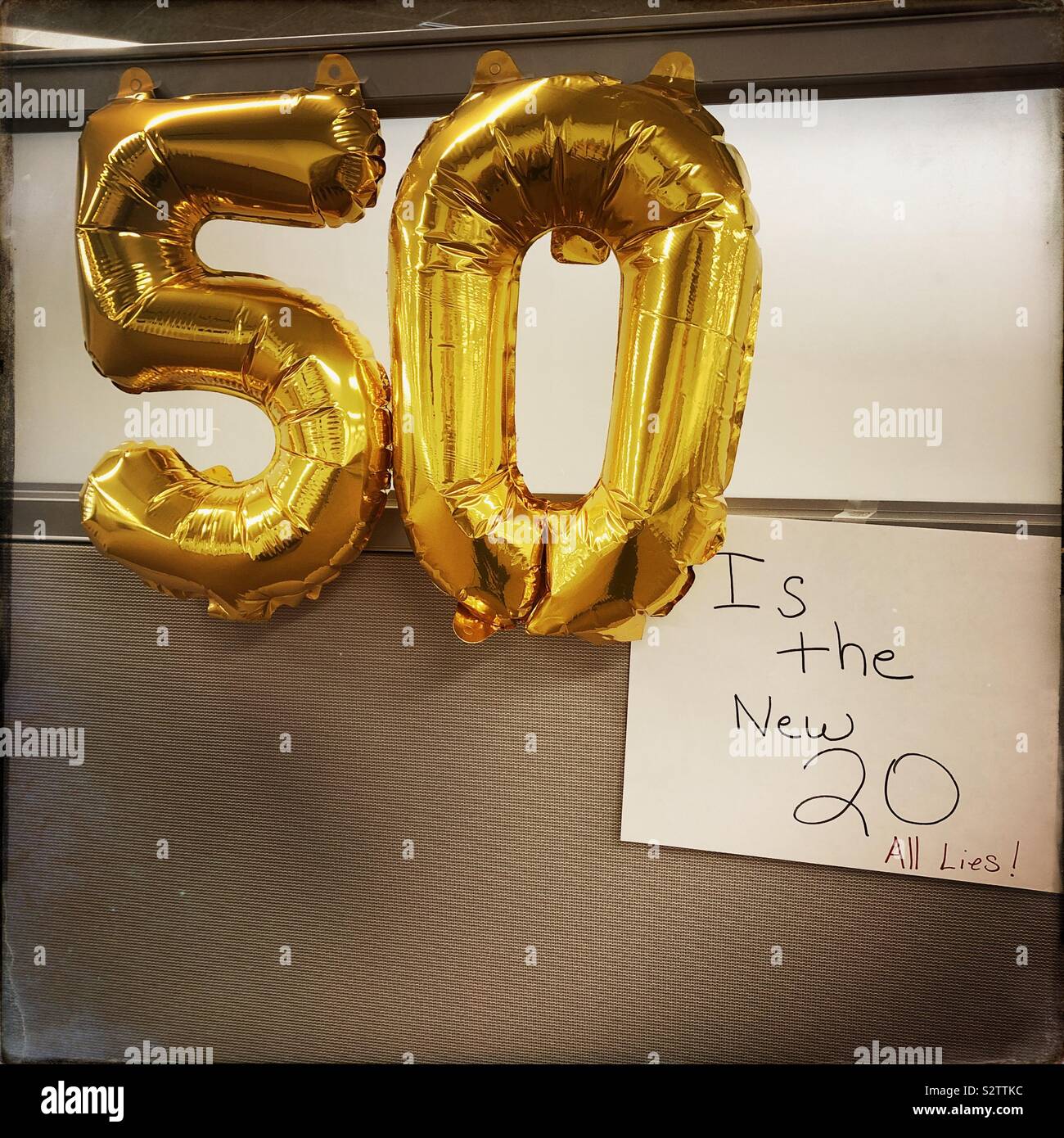 Fiftieth birthday celebration.  50 shaped balloons on a wall with a sign reading “is the new 20...all lies!”. - Smartphone Captured Stock Image