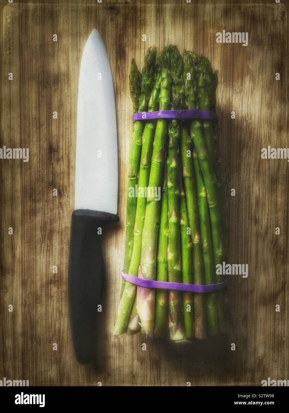 Fresh asparagus bunch on wooden cutting board with ceramic knife - Smartphone Captured Stock Image