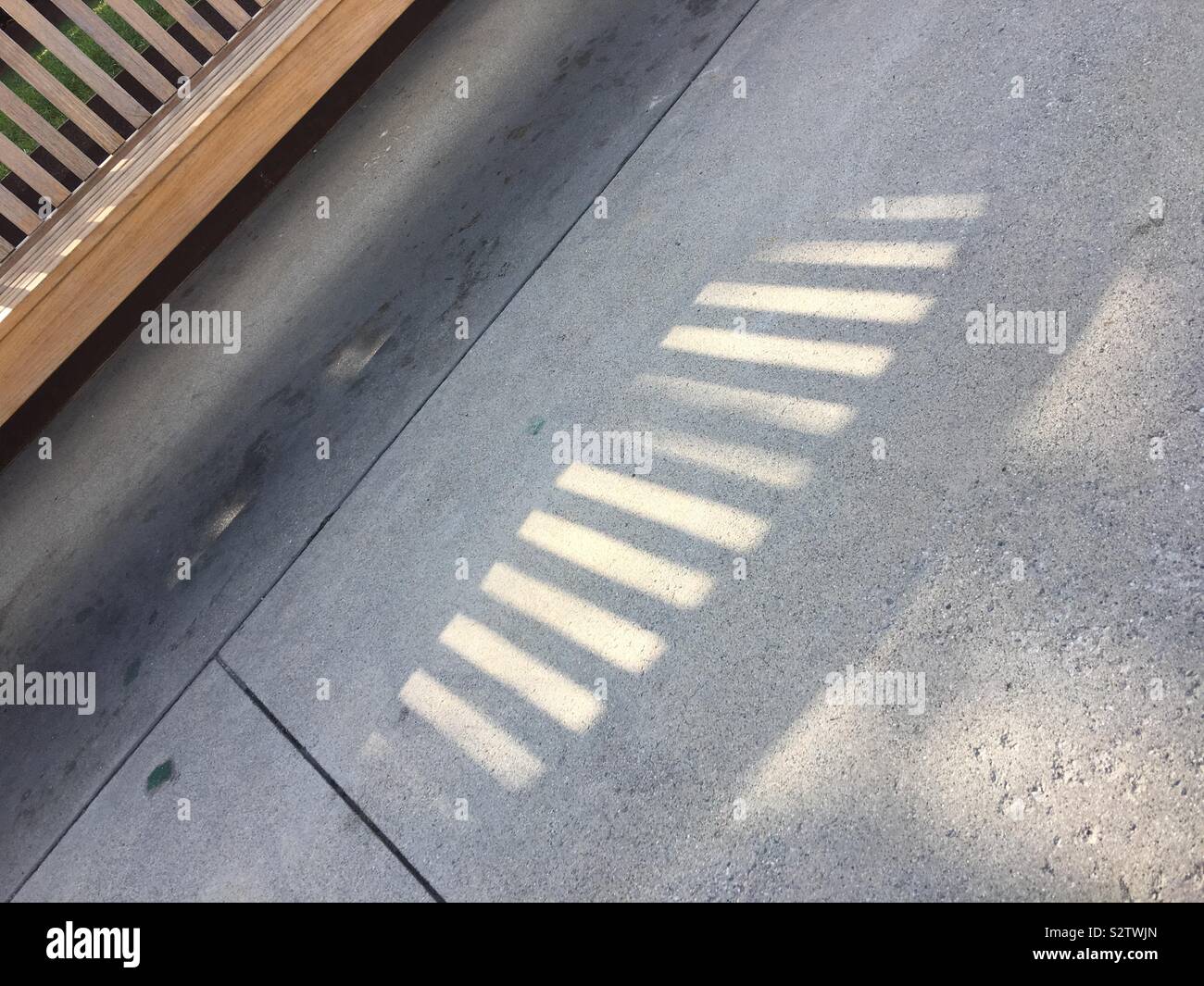Tilted image of shadow on cement pavement created by sun light behind a wooden bench - Smartphone Captured Stock Image