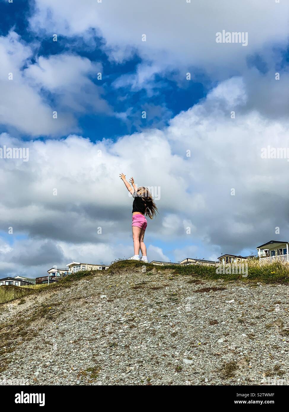 Young girl reaching for the sky while stood on a mound in Cornwall Stock Photo