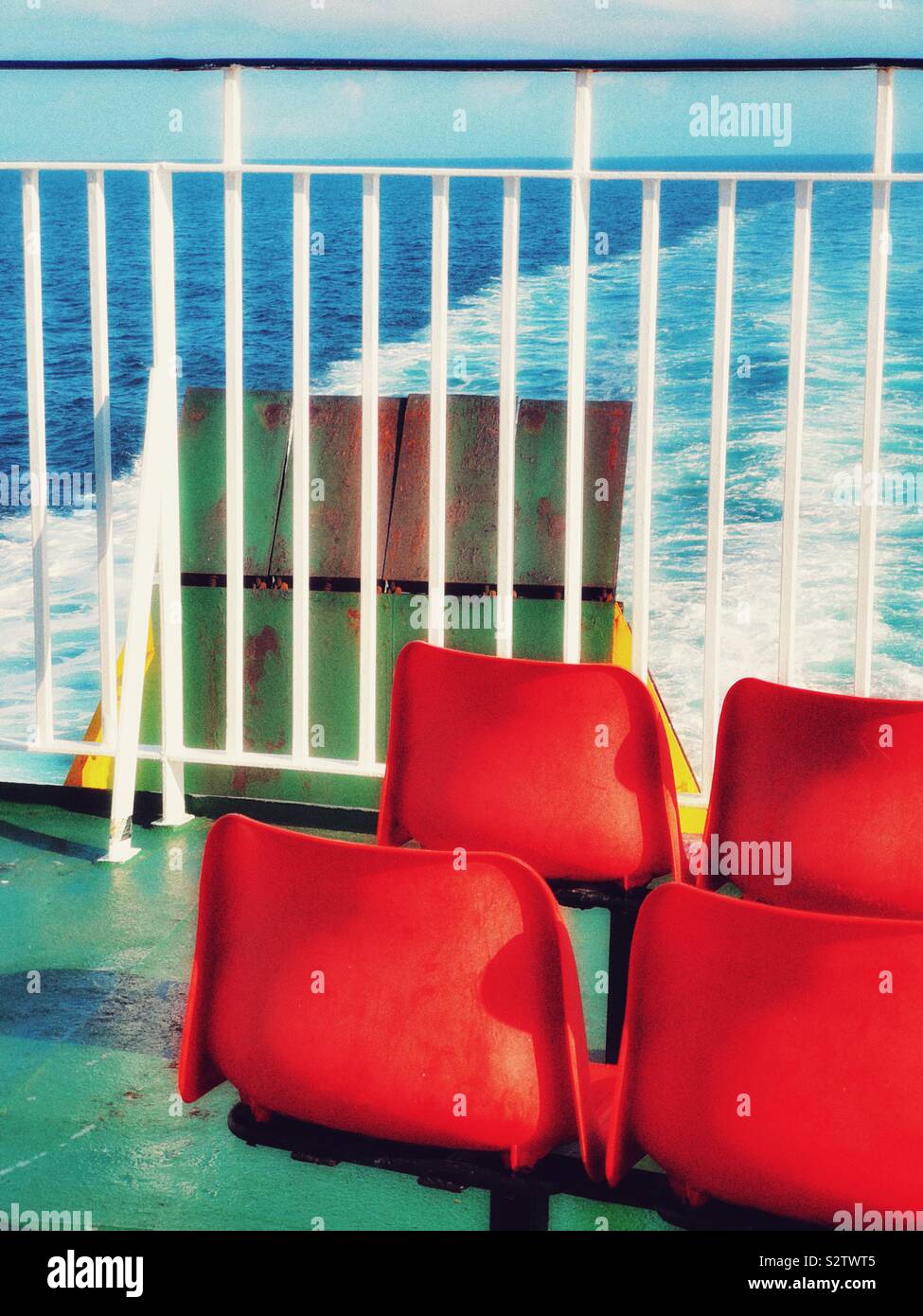 Empty red deck seats at stern of ship facing ramp and wake left in open sea - Smartphone Captured Stock Image