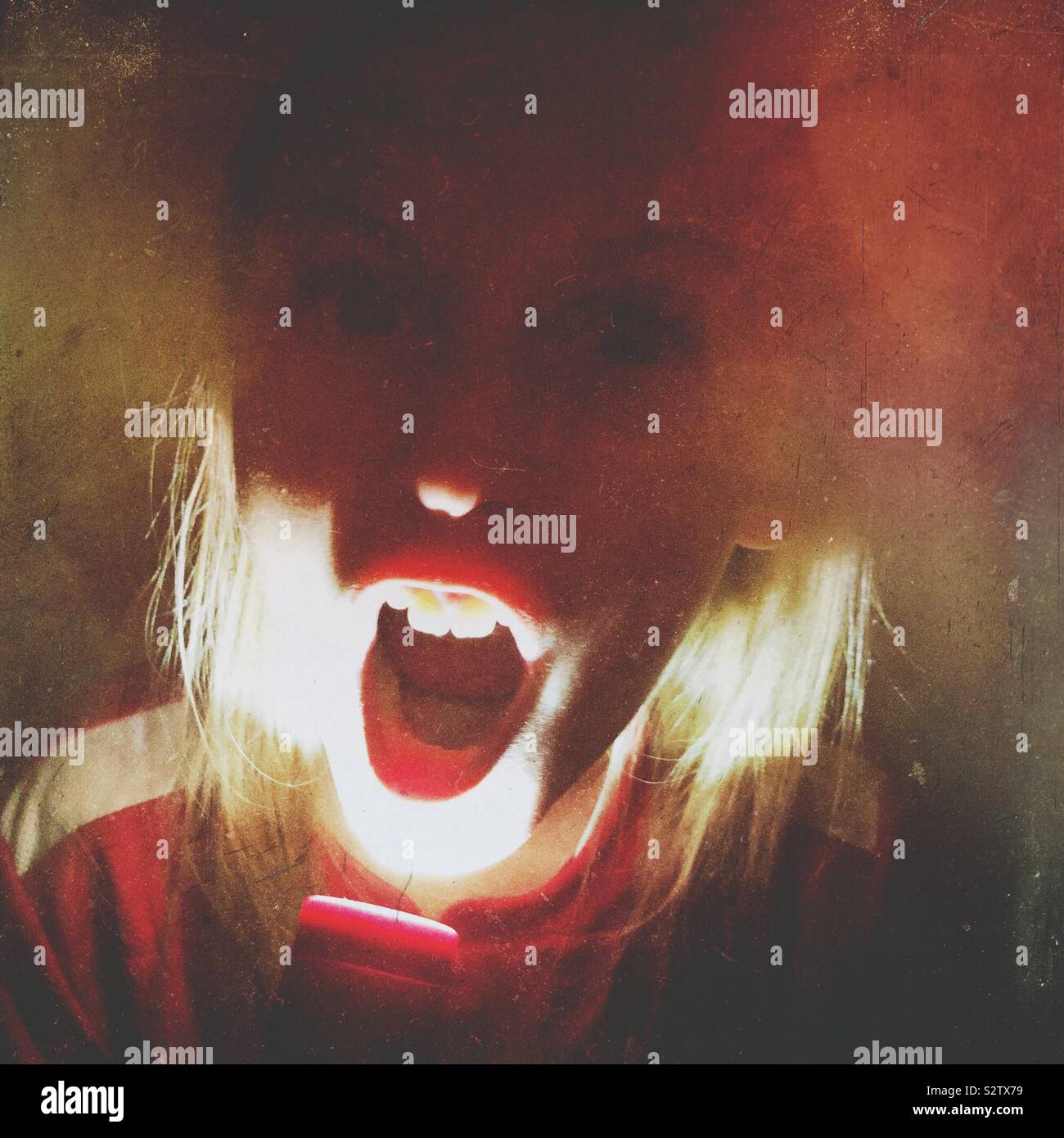 A girl shining a flashlight to her face.  She is making a scary face while telling spooky stories.  A Mextures filter has been used. - Smartphone Captured Stock Image