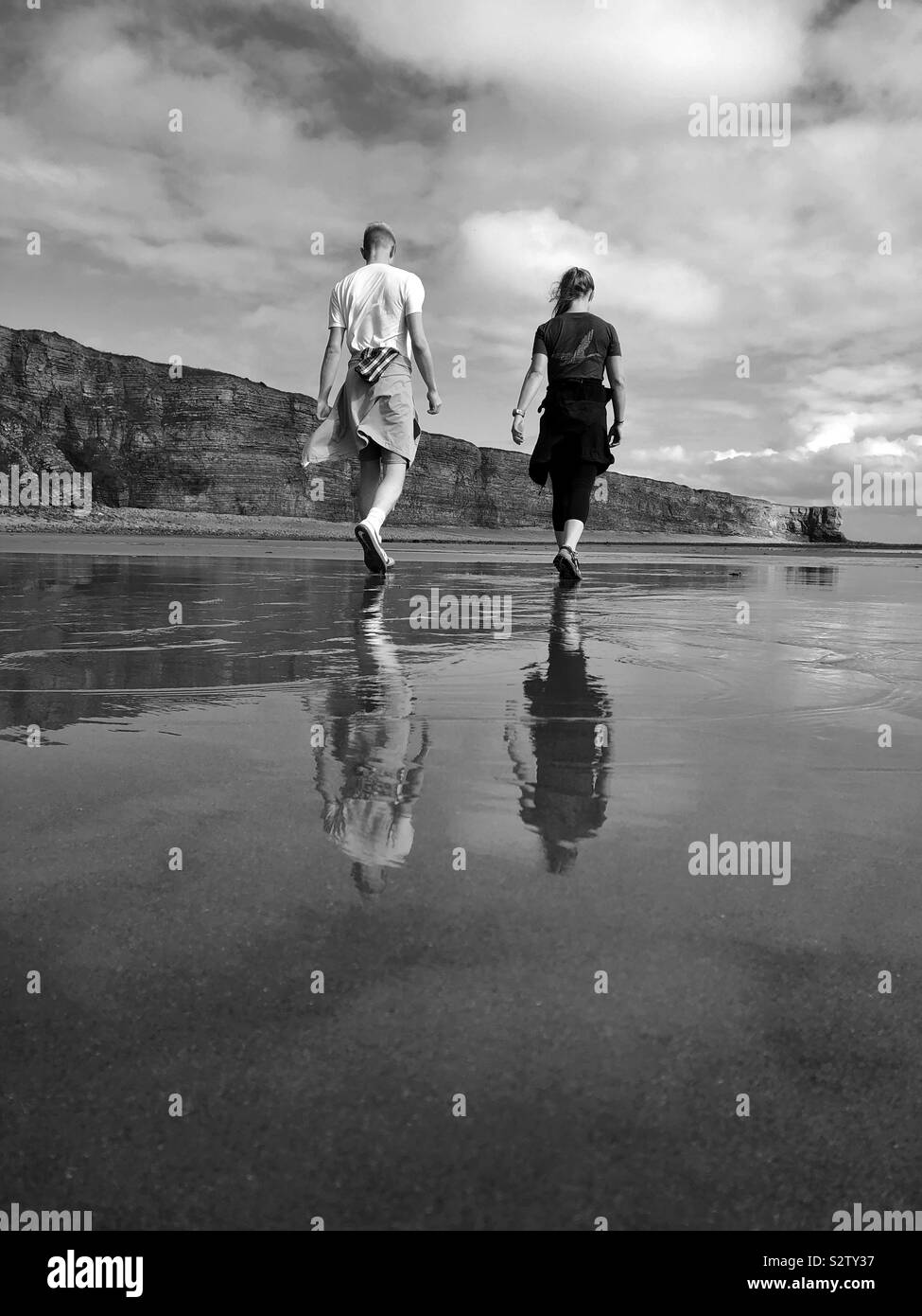 Two young people walking across a Welsh beach with reflections, August. Stock Photo