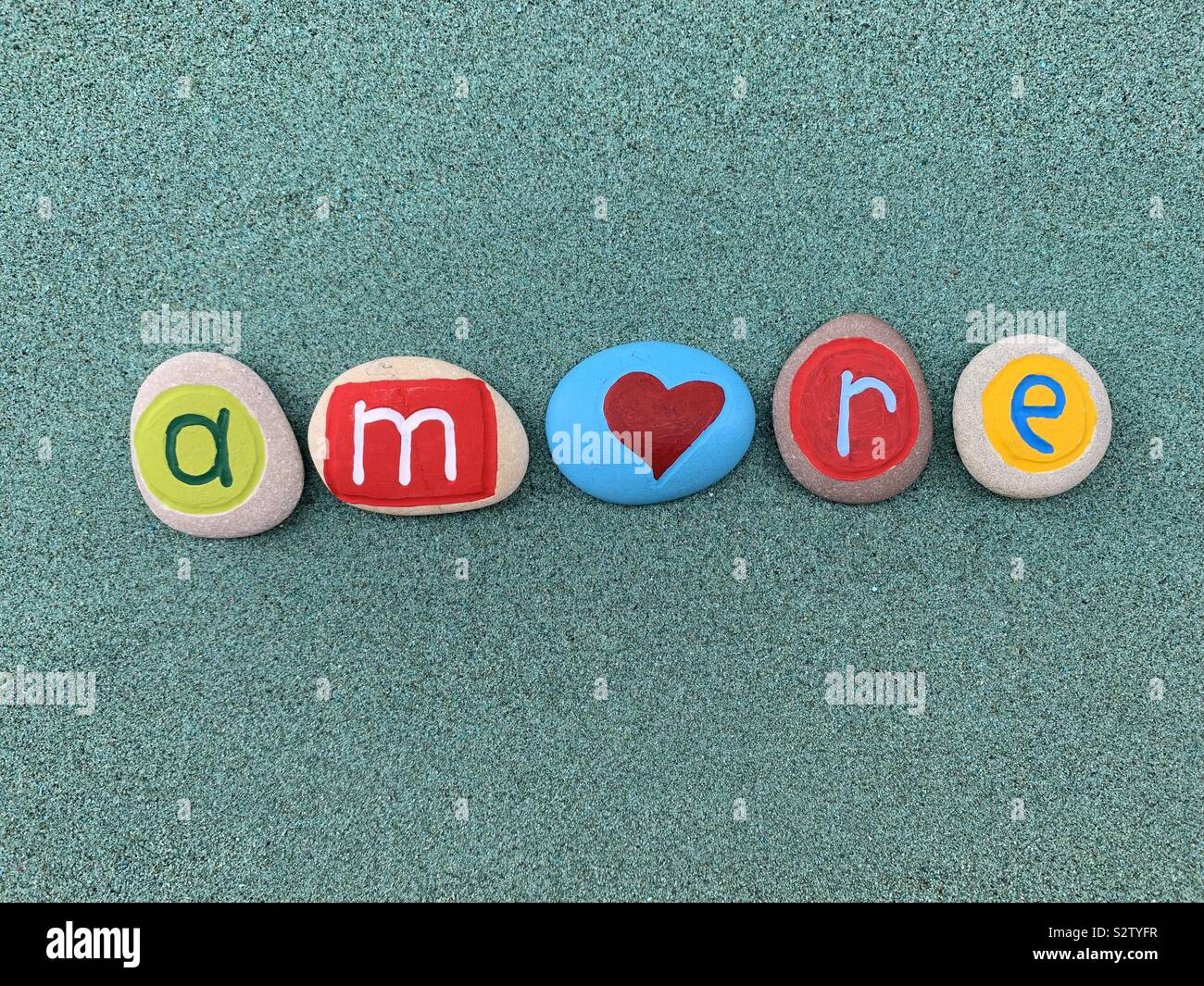 Amore, love word in italian language composed with creative painted stone letters over green sand Stock Photo