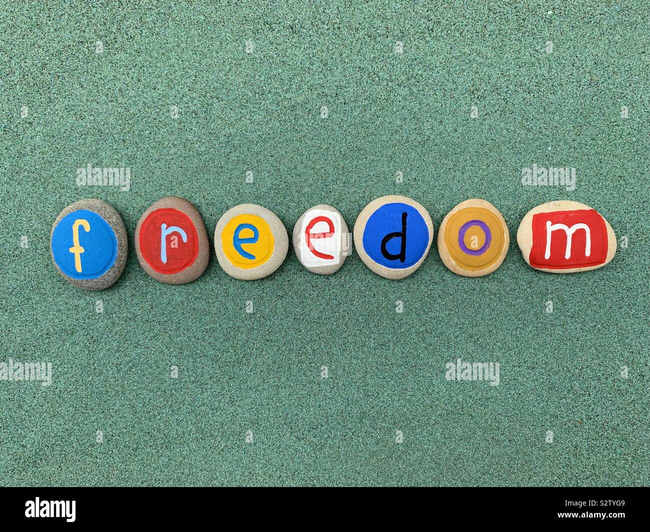 Freedom word composed with creative painted pebbles over green sand - Smartphone Captured Stock Image
